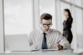 Office worker sitting at desk in office using laptop, while women talking phone in the background. Royalty Free Stock Photo