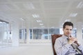 Office worker sitting in swivel chair hands clasped in empty office space