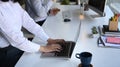 Office worker working on laptop and sitting with her colleague at office desk. Royalty Free Stock Photo