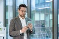 Office worker, young man in a suit standing indoors and using a tablet Royalty Free Stock Photo