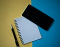 Office workplace minimal concept. Blank notebook with pencil, mobile phone on yellow and blue background Royalty Free Stock Photo