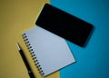 Office workplace minimal concept. Blank notebook with pencil, mobile phone on yellow and blue background Royalty Free Stock Photo