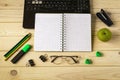 Office workplace with open laptop, notebook, marker, pencils, glasses, green apple on a light wooden table.