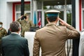 An officer in an official uniform stands with a man in a suit and greets NATO officials
