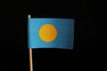 A official Flag of Palau on wooden stick on black background. Palau belongs to Oceania. Palau is island state