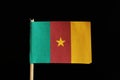 A official and original flag of Cameroon on toothpick on black background. It is a vertical tricolor of green, red and yellow with