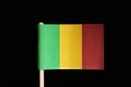 A official and original flag of Mali on toothpick on black background. Consists of a vertical tricolour of green, gold and red.