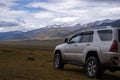 Offroad suv car on moutain plateau with mountains and rain clouds background. Summer vacation, travel concept. Royalty Free Stock Photo