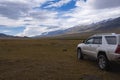 Offroad suv car on moutain plateau with mountains and rain clouds background. Summer vacation, travel concept. Royalty Free Stock Photo