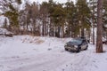 Offroad SUV `Jeep Grand Cherokee` 4x4 black color rides in the winter on the snow in the forest among the pines with a woman