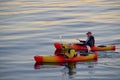 Two people paddle their colourful kayaks in the ocean at sunset