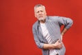 Oh, i need a massage! Portrait of a senior aged man having a back pain against a red background Royalty Free Stock Photo