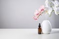 Oil diffuser with glass amber bottle and orchid flowers on white table