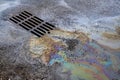 An oil or gasoline slick against the backdrop of an asphalt road flows into a storm drain. Environmental problems of Royalty Free Stock Photo