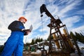 Oil man with laptop controlling work of pump jack. Royalty Free Stock Photo