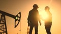 oil production. two silhouette workers work as a team next to an oil pump. business oil production production concept Royalty Free Stock Photo