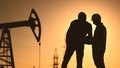 oil production. two silhouette workers work as a team next to an oil pump. business oil production production concept Royalty Free Stock Photo