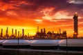 Oil refinery with numerous pipelines and storage tanks, spewing thick fumes into the sky, as a fiery sunset looms behind it Royalty Free Stock Photo