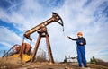 Oil worker in uniform and helmet working in an oilfield next to a pump jack on a sunny day Royalty Free Stock Photo