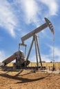 Oilfield pump jack out in summer red dirt field on bright day with shadow and a few whispy clouds in blue sky