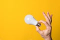 Ok gesture closeup hand holding white led lighting bulb against a yellow wide background banner with copyspace. concept Royalty Free Stock Photo