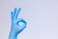 Ok sign is showed by left man hand in a blue medical glove on a white background. Okay