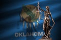 Oklahoma US state flag with statue of lady justice and judicial scales in dark room. Concept of judgement and punishment