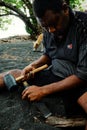 local artist carving a small wooden tribal statue in the black volcanic sand on the tropical sea ocean beach