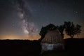 Old abandoned barn farm house with some trees behind it shot in the night against a starry sky with milky way galactic core seen