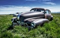 Old abandoned car in a garden surrounded by greenery with cars on the background under a blue sky Royalty Free Stock Photo