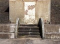 Old abandoned concrete shelter with a blocked door with cracked repaired steps and patched eroded walls in sunlight and shadow