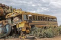 Old, abandoned, damaged school bus amid scrap metal at a salvage yard.