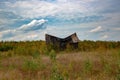 An old abandoned dilapidated house in a meadow covered with trees against a cloudy sky. Royalty Free Stock Photo
