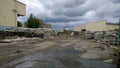 Old abandoned factory. Warehouse materials outdoors. Dirty broken road. Messy. Pits and puddles on the pavement. Overcast sky. Eco