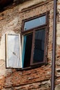 Old abandoned house facade with decaying brick wall and window hanging in a single hinge