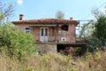 Old abandoned house with large terrace in front full of garbage and old washing machine surrounded with dense dry grass and trees