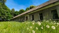 Old abandoned long house in poor condition. Bars and cracked panes in the windows. Around the tree and dandelions in the grass.