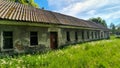 Old abandoned long house in poor condition. Bars and cracked panes in the windows. Around the tree and dandelions in the grass. Royalty Free Stock Photo