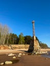 Old abandoned metal rusty lighthouse with a large stone foundation on the sea shore with a sandstone cliff. Shore stones