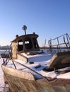 Old rusty boat moored to the shore in the winter froze on the river