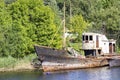 Old abandoned rusty small ship. Against the background of green overgrown bushes and trees