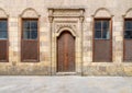 Old abandoned stone decorated bricks wall with arched wooden door and four shutter windows