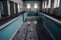 An old abandoned swimming pool. Wooden chair at the bottom. Dirty floor. Shabby walls. Blue tiles.