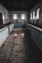 An old abandoned swimming pool. Wooden chair at the bottom. Dirty floor. Shabby walls. Blue tiles.