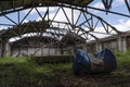 An old abandoned warehouse hangar with a ruined leaky roof and wooden floors, overgrown with grass inside. an old barrel