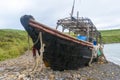 Old abandoned wooden fishing boat in blue color on the beach. A fishing net hangs from the sides