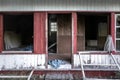 Old abandoned wooden house falling apart. Broken windows, scattered glass, white walls, red doors and window frames Royalty Free Stock Photo