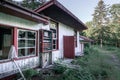 Old abandoned wooden house falling apart. Broken windows, scattered glass, white walls, red doors and window frames Royalty Free Stock Photo