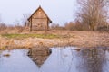 Old abandoned wooden house, a hut in the village with one small window is located near the pond, the house and the blue sky are re Royalty Free Stock Photo