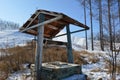 Old abandoned wooden well on a background of dry brown grass and white snow of snowboarding resort in mountains, Russia. Royalty Free Stock Photo